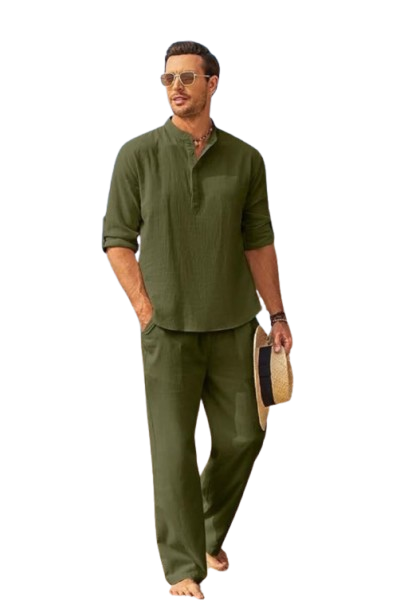 Man in olive green linen outfit walking on beach with sunglasses and straw hat.